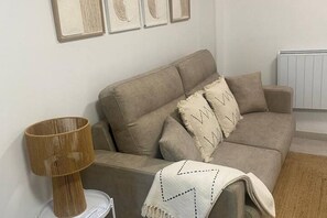 A neutral-toned living room with a sofa, a lamp, and a radiator. - 102B Poniente Mágico by R2R Consulting (Gijón)