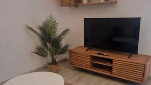 A modern living room with a flat-screen TV on a wooden cabinet, a round white table, and a potted palm plant. - 102B Poniente Mágico by R2R Consulting (Gijón)
