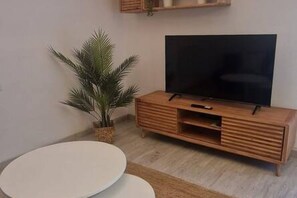 A modern living room with a flat-screen TV on a wooden cabinet, a round white table, and a potted palm plant. - 102B Poniente Mágico by R2R Consulting (Gijón)
