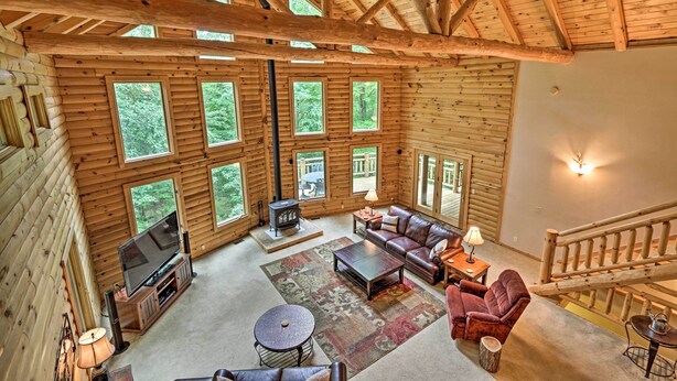 A log cabin interior with a fireplace, leather sofa, and large windows.