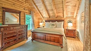 A wooden cabin bedroom with a large bed, dresser, and nightstands.