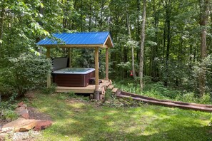 Een hottub met een houten terras en een blauw dak, omringd door een bos.