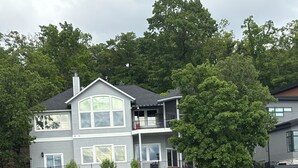 A two-story house with a dock extending into a body of water, surrounded by trees and a well-maintained lawn. - Lakefront property w dock & amazing sunsets  (Sunrise Beach)