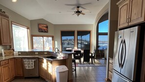 A modern kitchen with wooden cabinets, a stainless steel refrigerator, and a dining area with a view. - Lakefront property w dock & amazing sunsets  (Sunrise Beach)