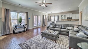 A spacious living room with a large sectional sofa, a coffee table, and a patterned rug. There is a dining area with a kitchen in the background. - Spacious Mccalla Home w/ Yard & Game Room! (McCalla)