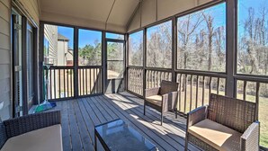 A covered porch with a wooden deck, wicker furniture, and large windows offering a view of trees and a distant building. - Spacious Mccalla Home w/ Yard & Game Room! (McCalla)
