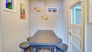 A dining area with a long table and four chairs, a ceiling fan, and wall art including a fish and a lighthouse. - Steps to Beach & Bites: Catalina Island Retreat! (Avalon)
