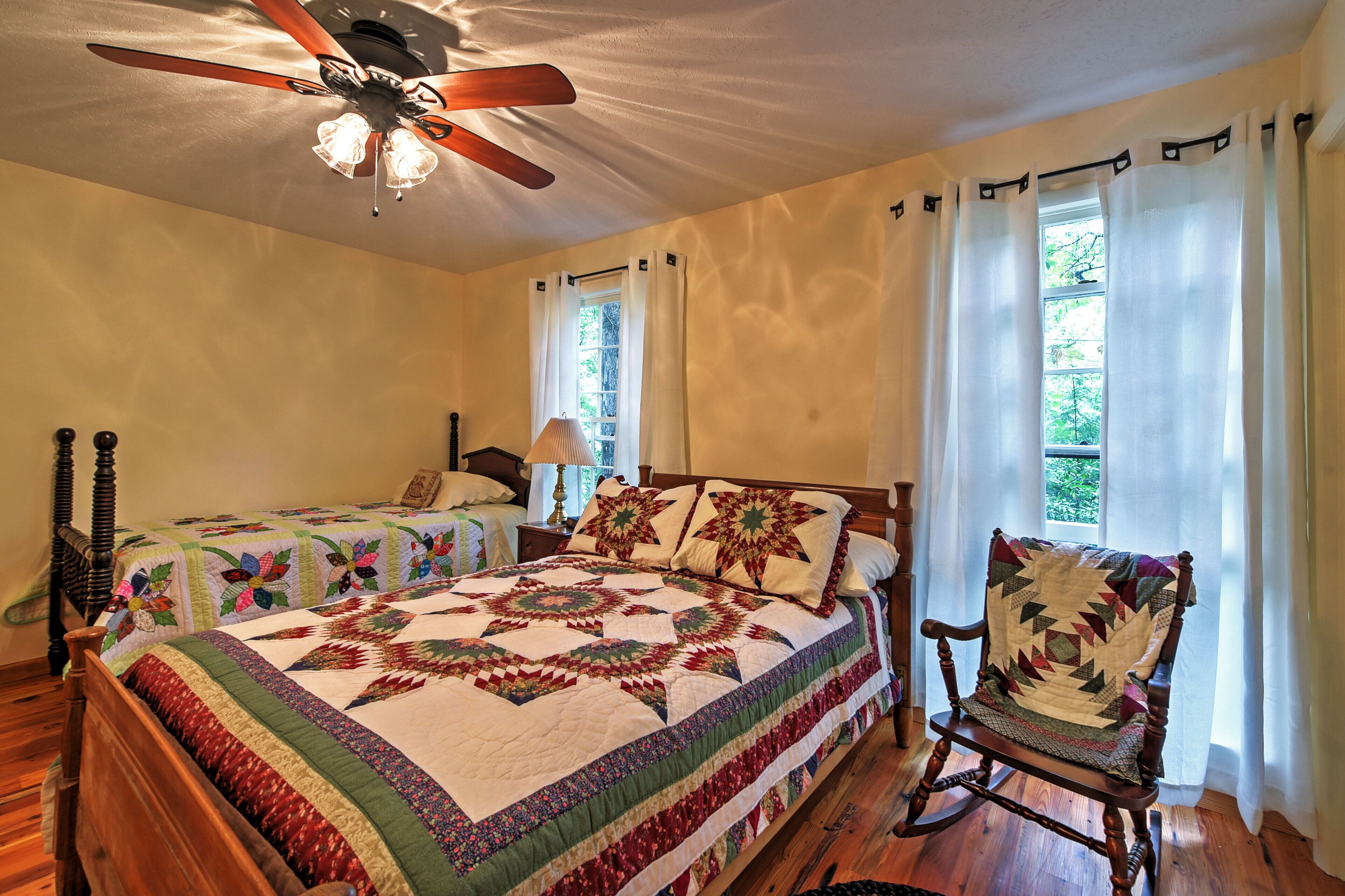 A bedroom with two beds, a rocking chair, a ceiling fan, and a window with curtains.