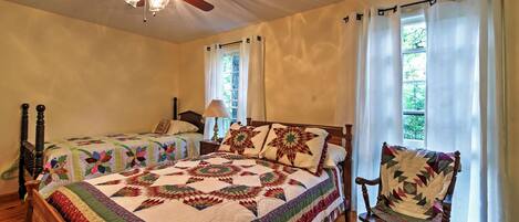 A bedroom with two beds, a rocking chair, a ceiling fan, and a window with curtains.