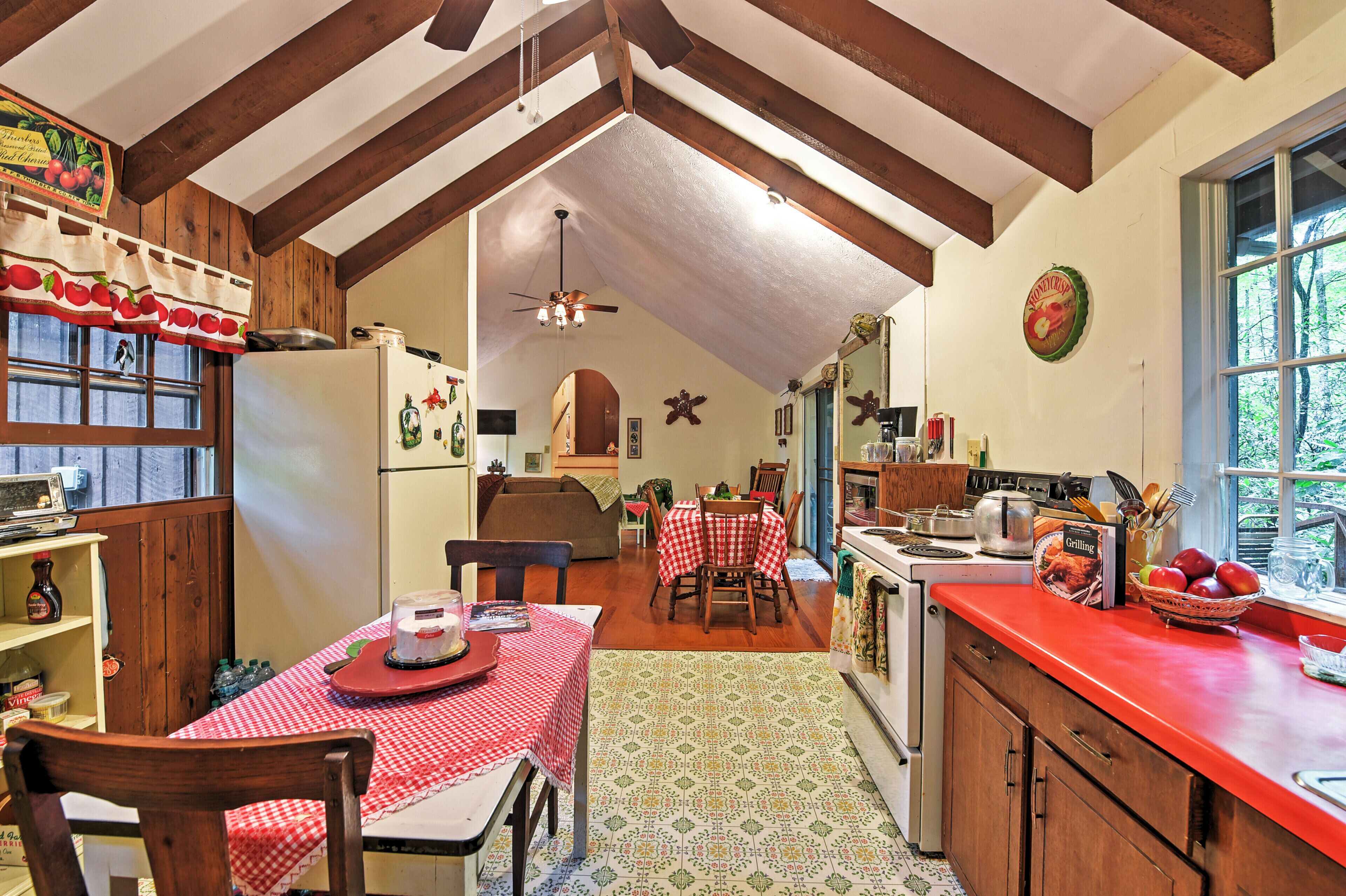 A kitchen with a red countertop, wooden cabinets, and a dining area with a red and white checkered tablecloth.