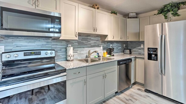 A modern kitchen with stainless steel appliances, white cabinetry, and a tiled backsplash. - Inviting Apartment < 2 Mi to Riviera Beach! (West Palm Beach)