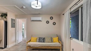 A living room with a sofa, a ceiling light, an air conditioner, and decorative wall art. - Inviting Apartment < 2 Mi to Riviera Beach! (West Palm Beach)