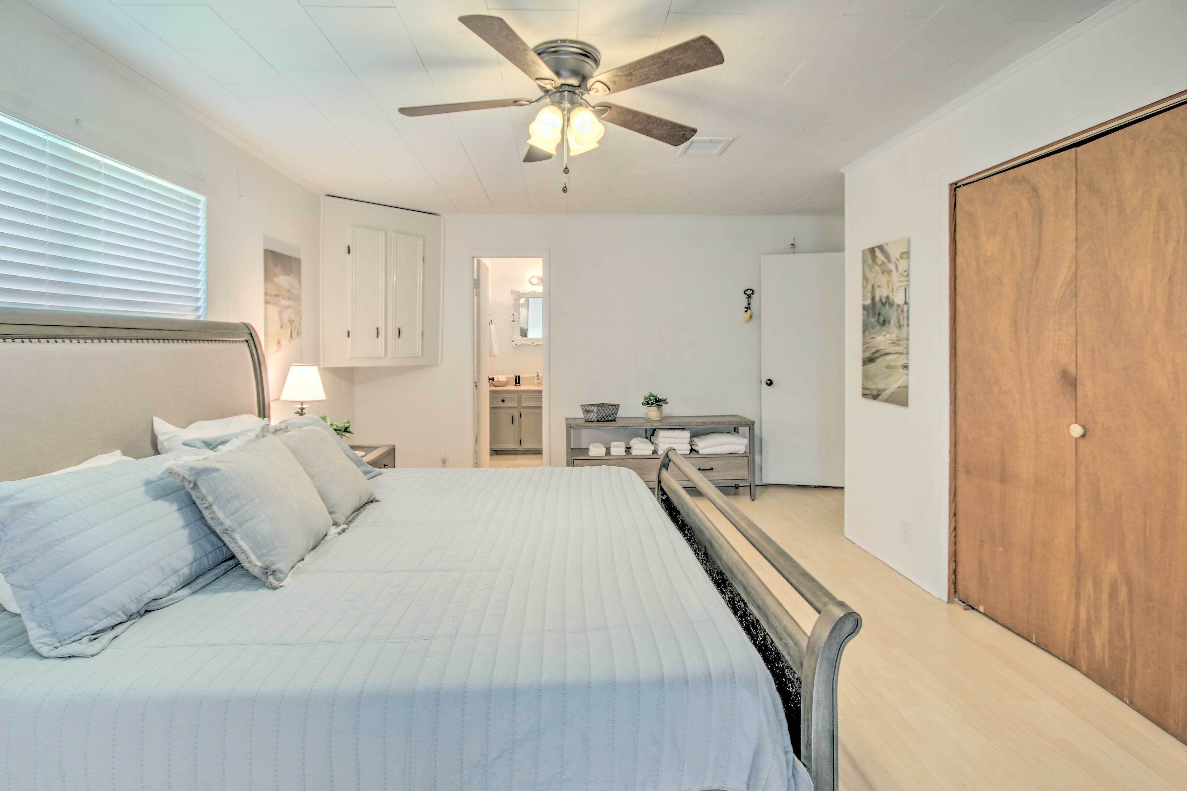 A bedroom with a bed, a ceiling fan, a wooden door, and a small bathroom visible through an open door.