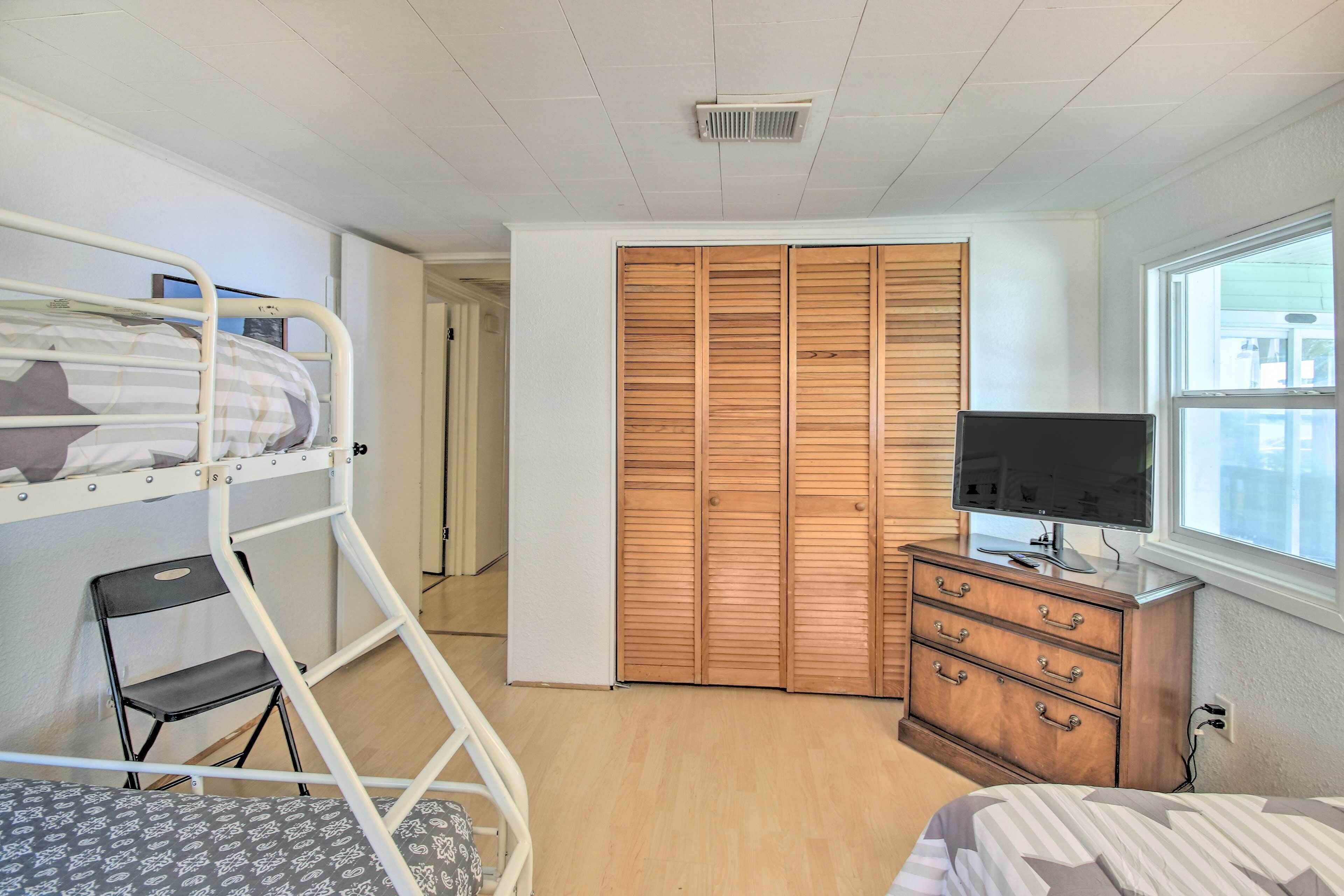 A room with bunk beds, a wooden wardrobe, a dresser, a television, and a window.