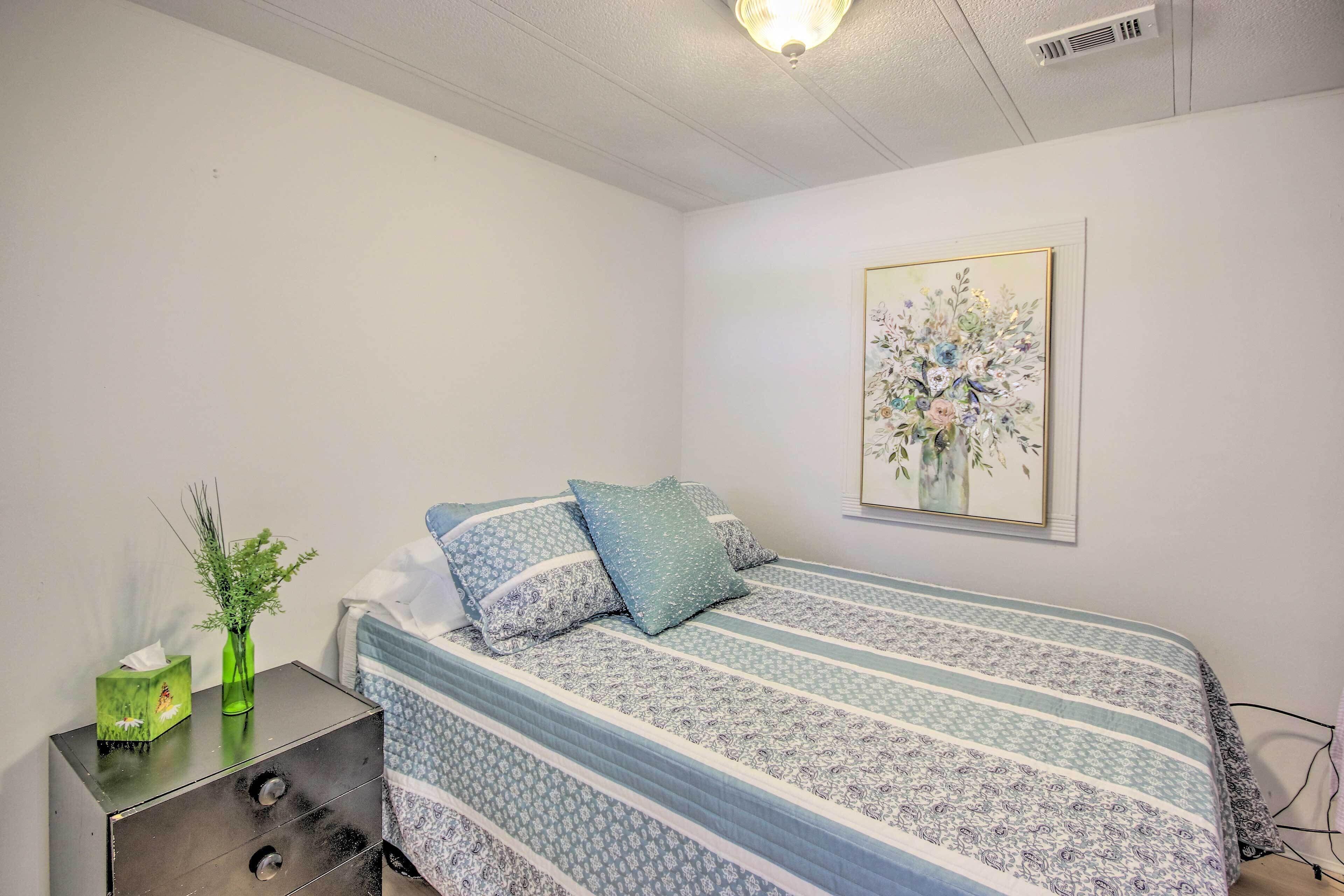A bedroom with a bed, a nightstand, a vase with plants, and a floral painting on the wall.