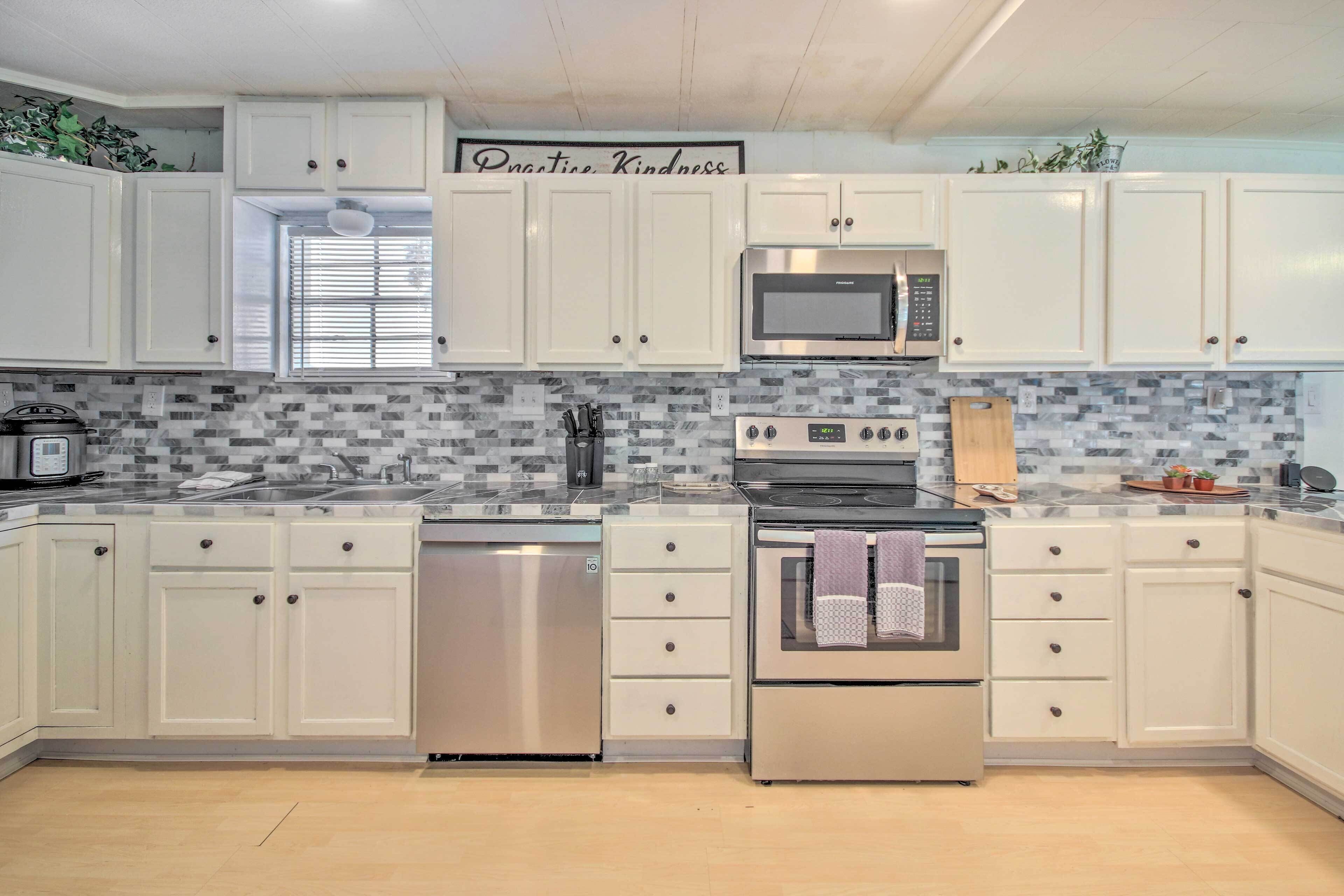 A kitchen with white cabinets, a stainless steel refrigerator, a microwave, an oven, and a dishwasher.