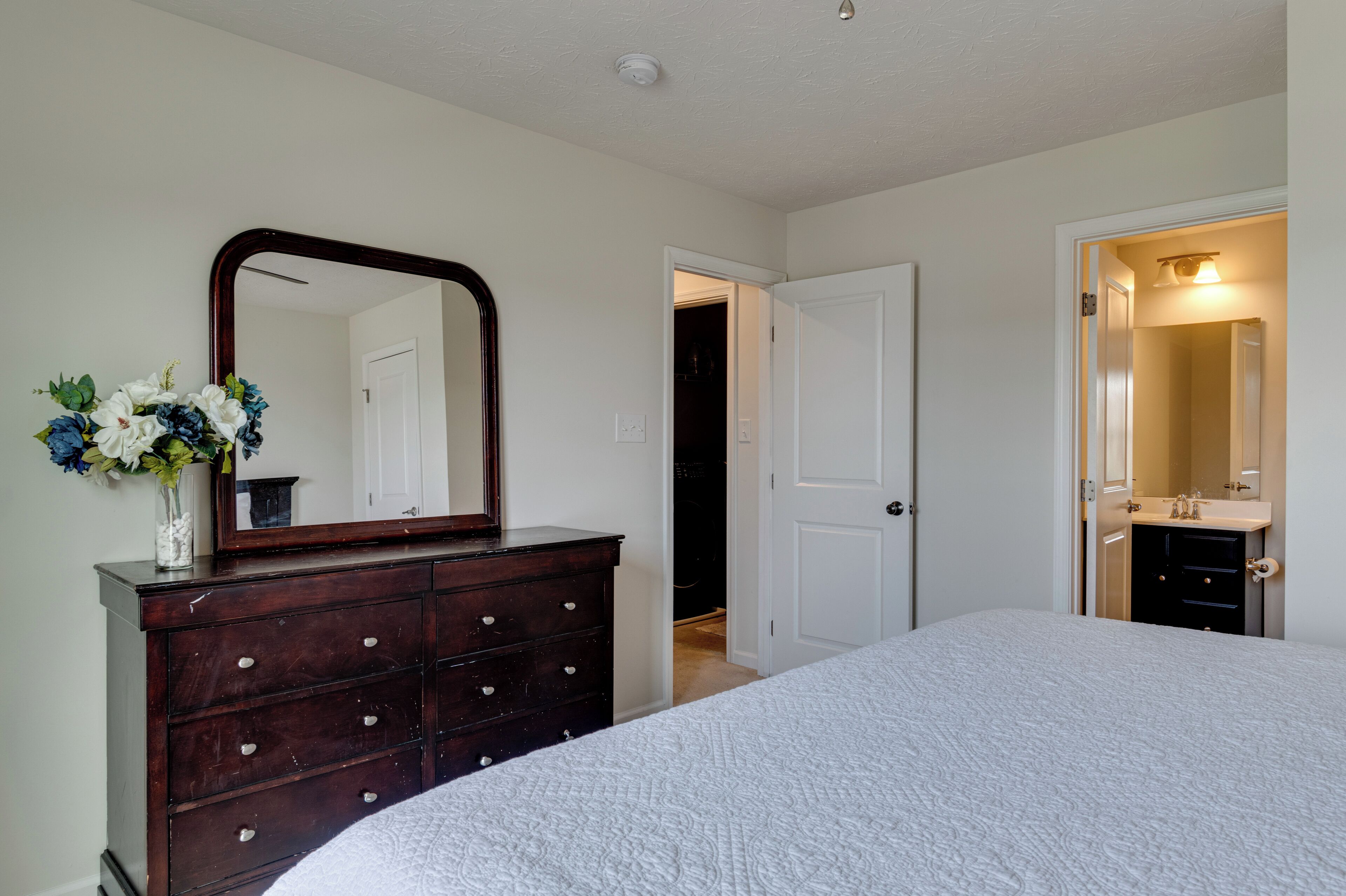 A bedroom with a large bed, a dresser with a mirror, and a door leading to a bathroom.