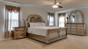 A bedroom with a large bed, a dresser, a vanity with a mirror, and a ceiling fan. - Spacious Home w/ Fireplace - Near Golf! (Brownsburg)