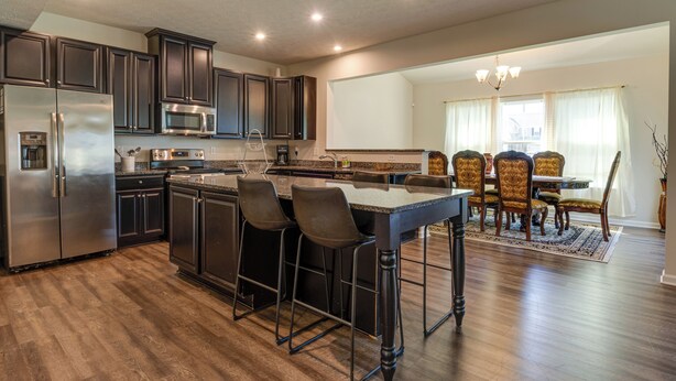A modern kitchen with dark cabinets, stainless steel appliances, and a bar area with stools. - Spacious Home w/ Fireplace - Near Golf! (Brownsburg)