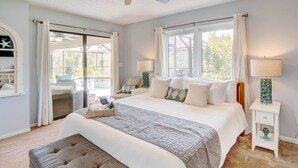 A bedroom with a large bed, a ceiling fan, a window with curtains, a nightstand with a lamp, and a view of the outside. - Punta Gorda Canal Home w/ Private Pool! (Punta Gorda)
