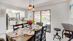 A dining area with a wooden table set for four, a vase of flowers, and a view of the kitchen and outside. - Punta Gorda Canal Home w/ Private Pool! (Punta Gorda)