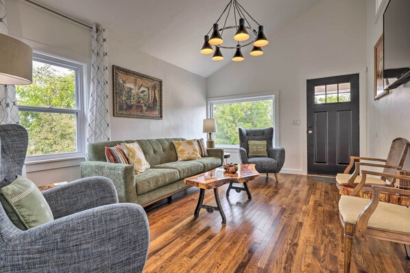 A spacious living room with a green sofa, grey armchairs, a wooden coffee table, and a black door. - Fredericksburg Getaway w/ Covered Deck & Fire Pit! (Fredericksburg)