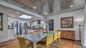 Una cocina moderna con una isla central, una zona de comedor con una mesa larga y sillas amarillas, y un techo con un diseño original.