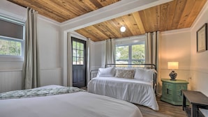 Un dormitorio con dos camas, techo de madera, una mesita de noche verde y una ventana con cortinas.