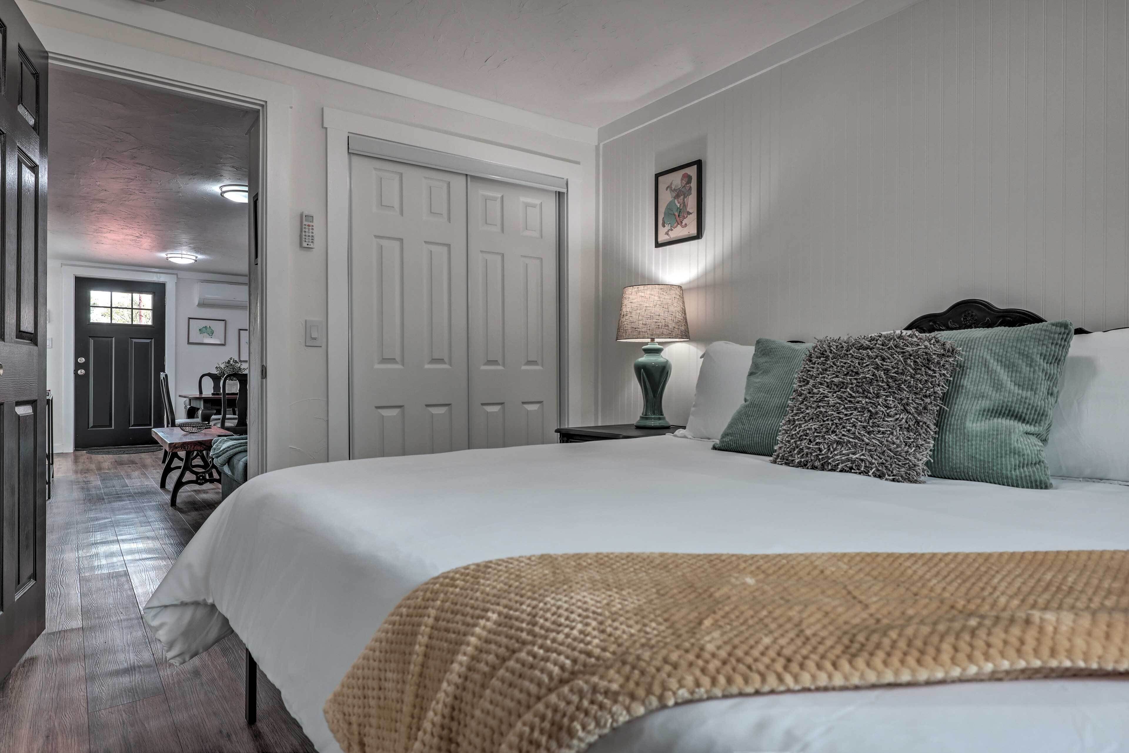 A bedroom with a large bed, a bedside table with a lamp, and a door leading to another room.