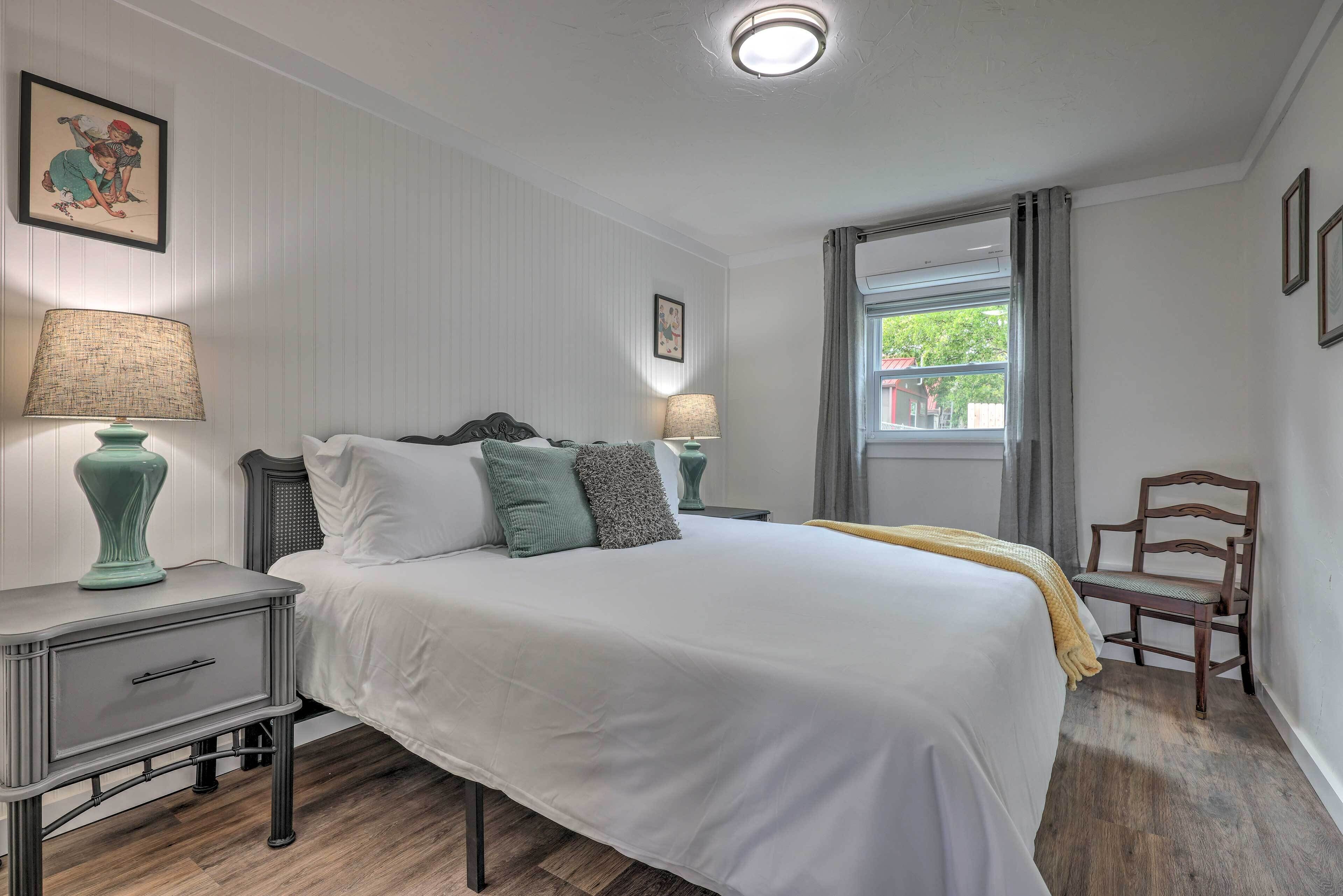 Een keurig opgemaakt slaapkamer met een groot bed, twee nachtkastjes, een stoel en een raam met gordijnen.