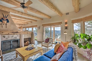 A spacious living room with a fireplace, wooden beams, large windows, and comfortable seating.