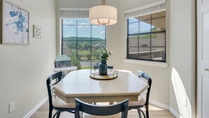 Un coin repas comprenant une table ronde, quatre chaises, un luminaire suspendu et de grandes fenêtres donnant sur l’extérieur.