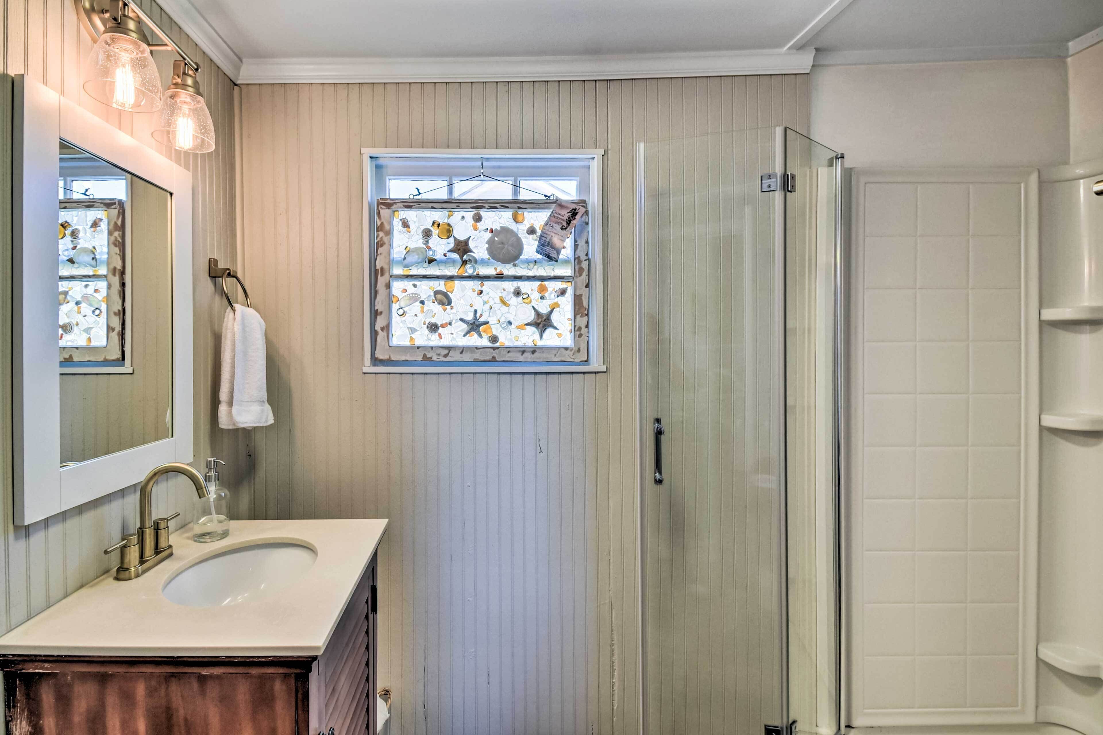 A bathroom with a sink, mirror, and a window with a decorative view.