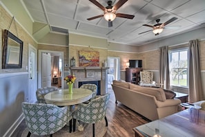 A spacious living room with a fireplace, a dining area with patterned chairs, and a ceiling fan. - Cozy Currituck Home w/ Fire Pit Near Ferry! (Currituck)