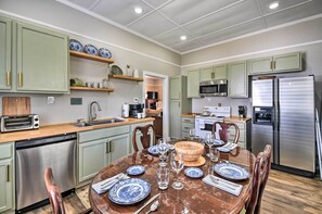 A modern kitchen with green cabinets, stainless steel appliances, and a dining area with a wooden table set for four. - Cozy Currituck Home w/ Fire Pit Near Ferry! (Currituck)