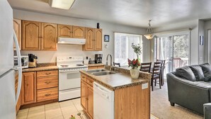 A kitchen with wooden cabinets, a white stove, and a dishwasher. There is a dining area with a gray couch and a dining table. - Peaceful Alaskan Escape: 13 Mi to Fairbanks! (Fairbanks)