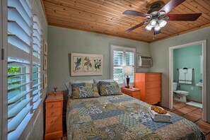 A bedroom with a bed, a ceiling fan, a window with blinds, a dresser, and a bathroom visible through an open door. - Palm Harbor Vacation Rental, Walk to Crystal Beach (Crystal Beach)