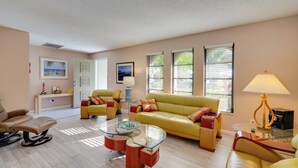 A living room with a yellow sofa, a glass coffee table, and a beige armchair. - Coastal Retreat w/ Grill: 4 Mi to Dtwn Cape Coral! (Cape Coral)