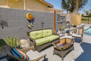 A patio area with a wicker sofa, a glass-top coffee table, and wicker chairs. - Pool & Spa: Palm Desert Home Near Golf! (Palm Desert)