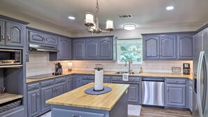 A modern kitchen with grey cabinets, a wooden island, stainless steel appliances, and a window providing natural light.