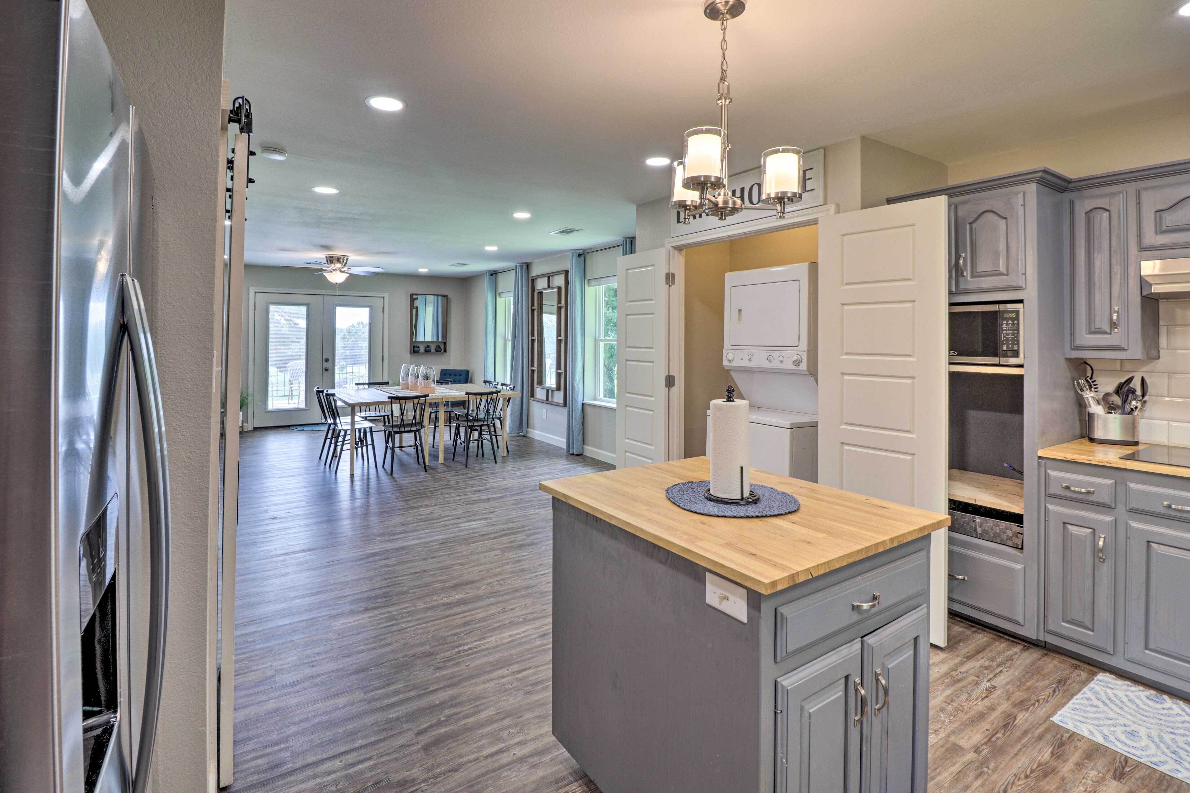 A modern kitchen with grey cabinets, a wooden countertop, and a central island. There is a dining area with a table and chairs in the background.