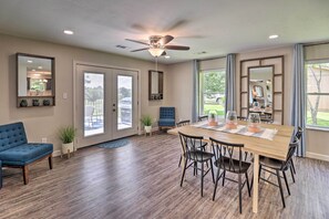 A spacious dining area with a wooden table and chairs, a ceiling fan, and large windows offering views of the outdoors.