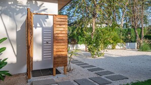A wooden door with a metal grill, a gravel pathway, and a small tree in a garden area. - Casa Prema | Modern 3BR Home in Playa Grande (Cabo Velas)