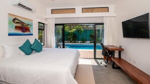 A bedroom with a large bed, a desk, and a TV. There is a sliding glass door leading to a pool area. - Casa Prema | Modern 3BR Home in Playa Grande (Cabo Velas)