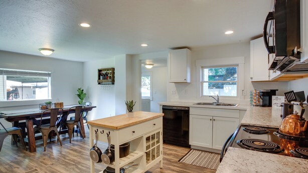 A modern kitchen with wooden flooring, white cabinetry, a built-in stove, and a dining area with a wooden table and chairs. - Adorable Coeur D'alene Home < 2 Mi to Lake! (Coeur d'Alene)