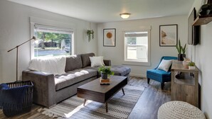A living room with a gray sofa, a blue chair, a wooden coffee table, and a patterned rug. - Adorable Coeur D'alene Home < 2 Mi to Lake! (Coeur d'Alene)