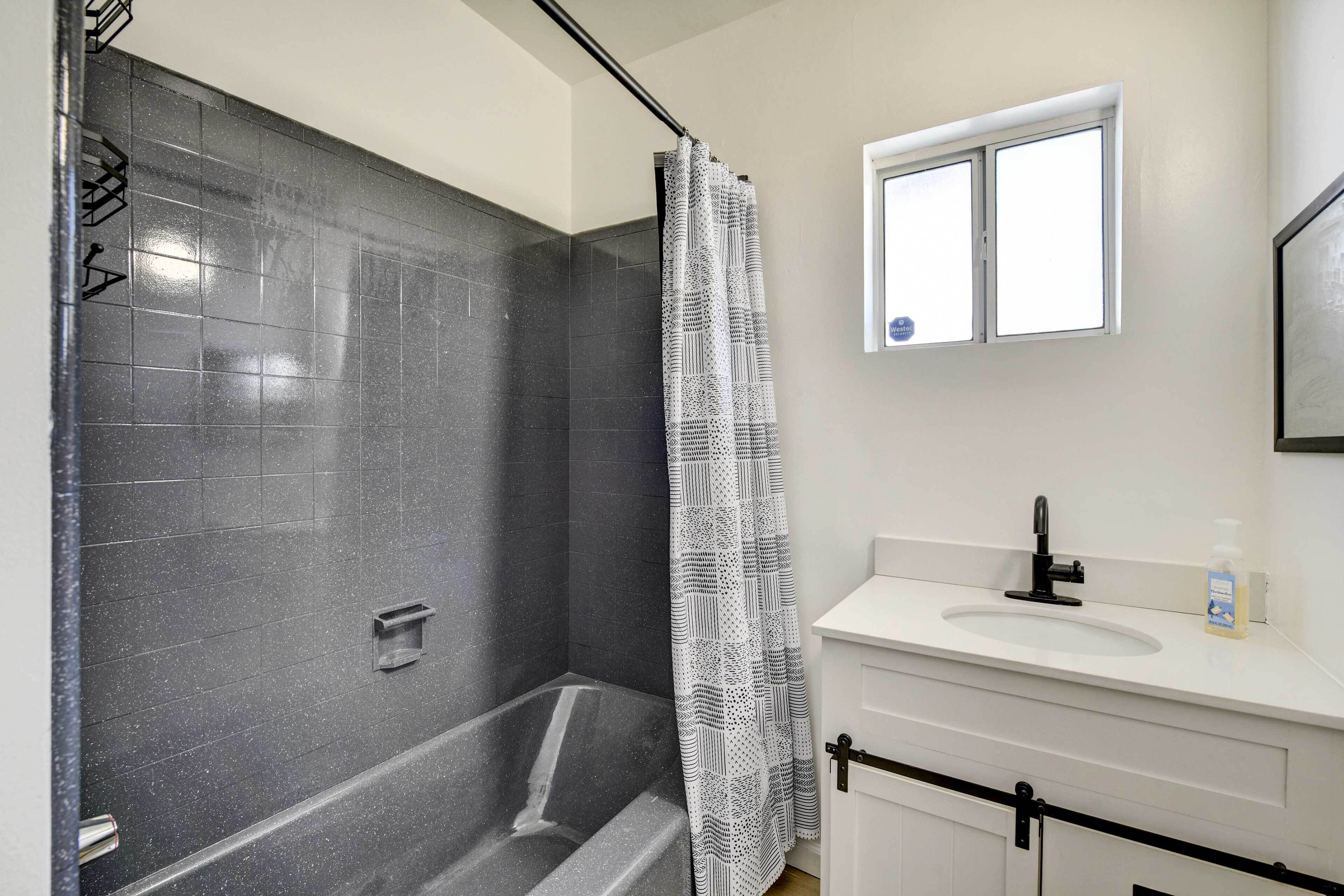 A modern bathroom with a shower, a white sink, and a window.