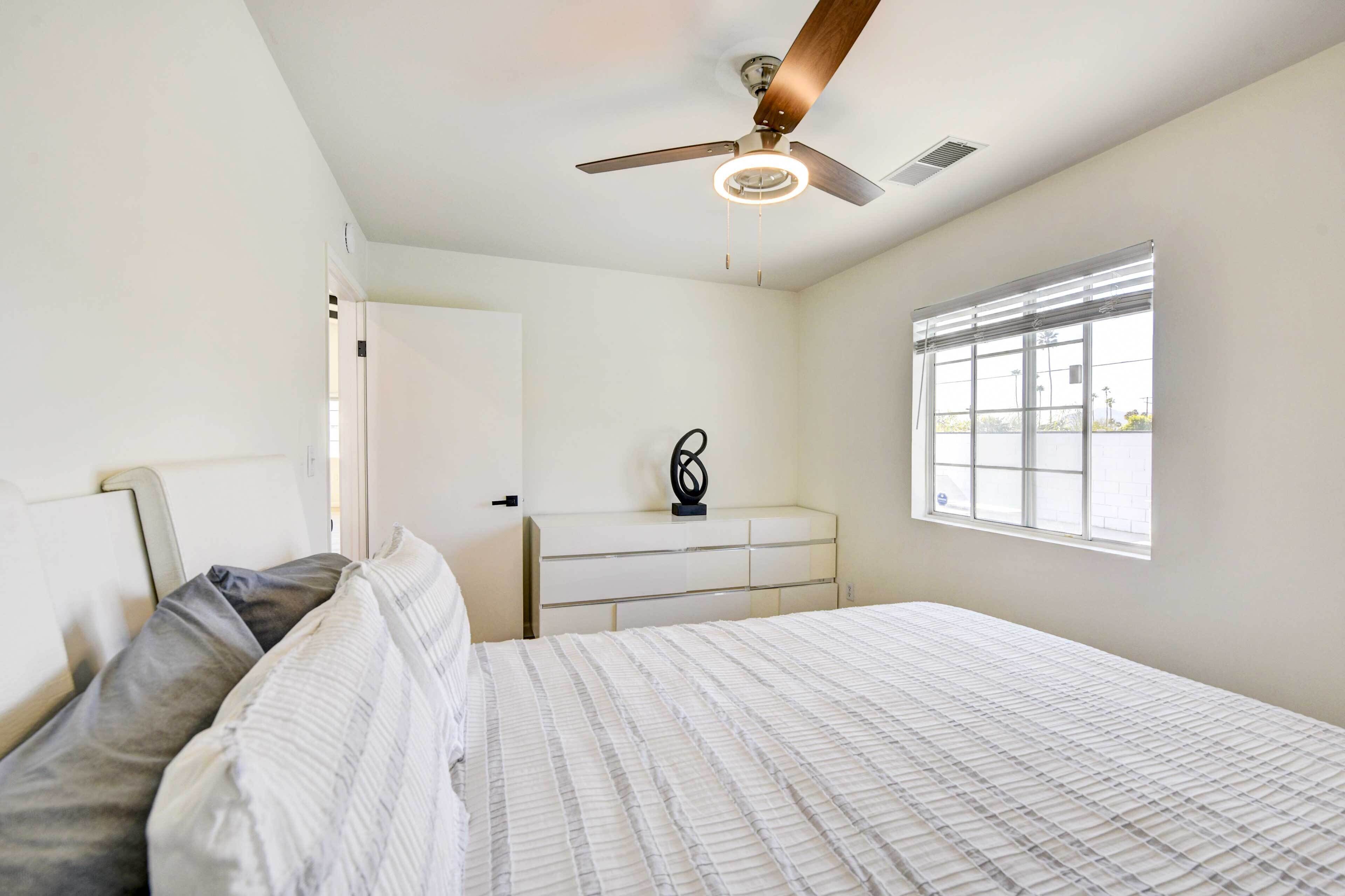 A bedroom with a bed, a dresser, a ceiling fan, and a window.