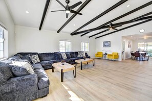 Un salon spacieux avec un canapé d’angle, deux tables basses en bois et un ventilateur de plafond.