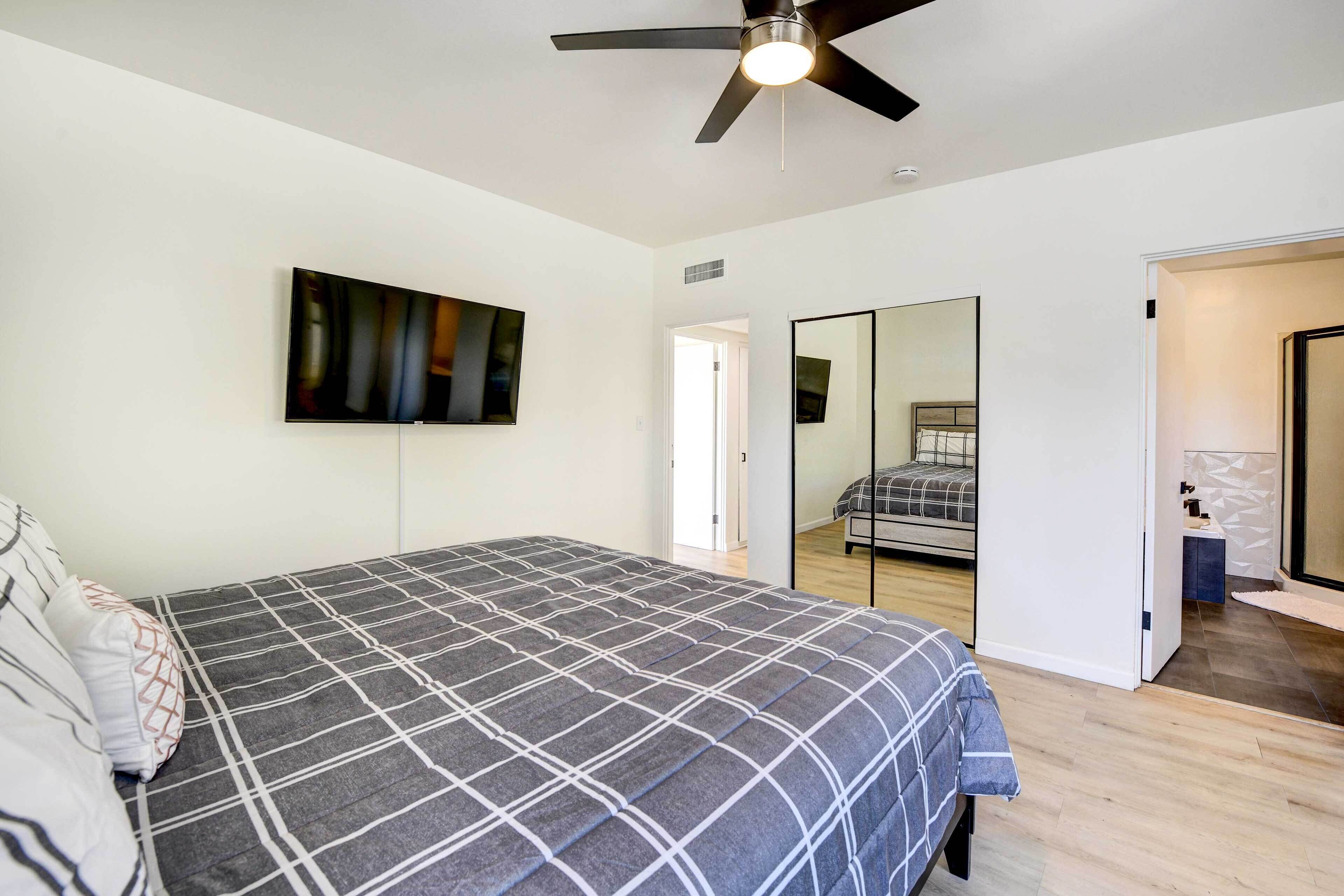 A bedroom with a bed, a ceiling fan, a large mirror, and a door leading to another room.